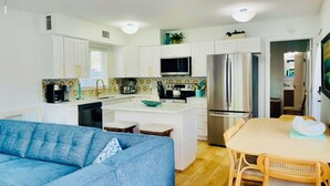 A modern kitchen with white cabinets, a central island, stainless steel appliances, and a dining area with a table and chairs. - Steps to the Beach, No Car Needed, Completely Permitted Remodel + King Size Bed! (Indian Rocks Beach)