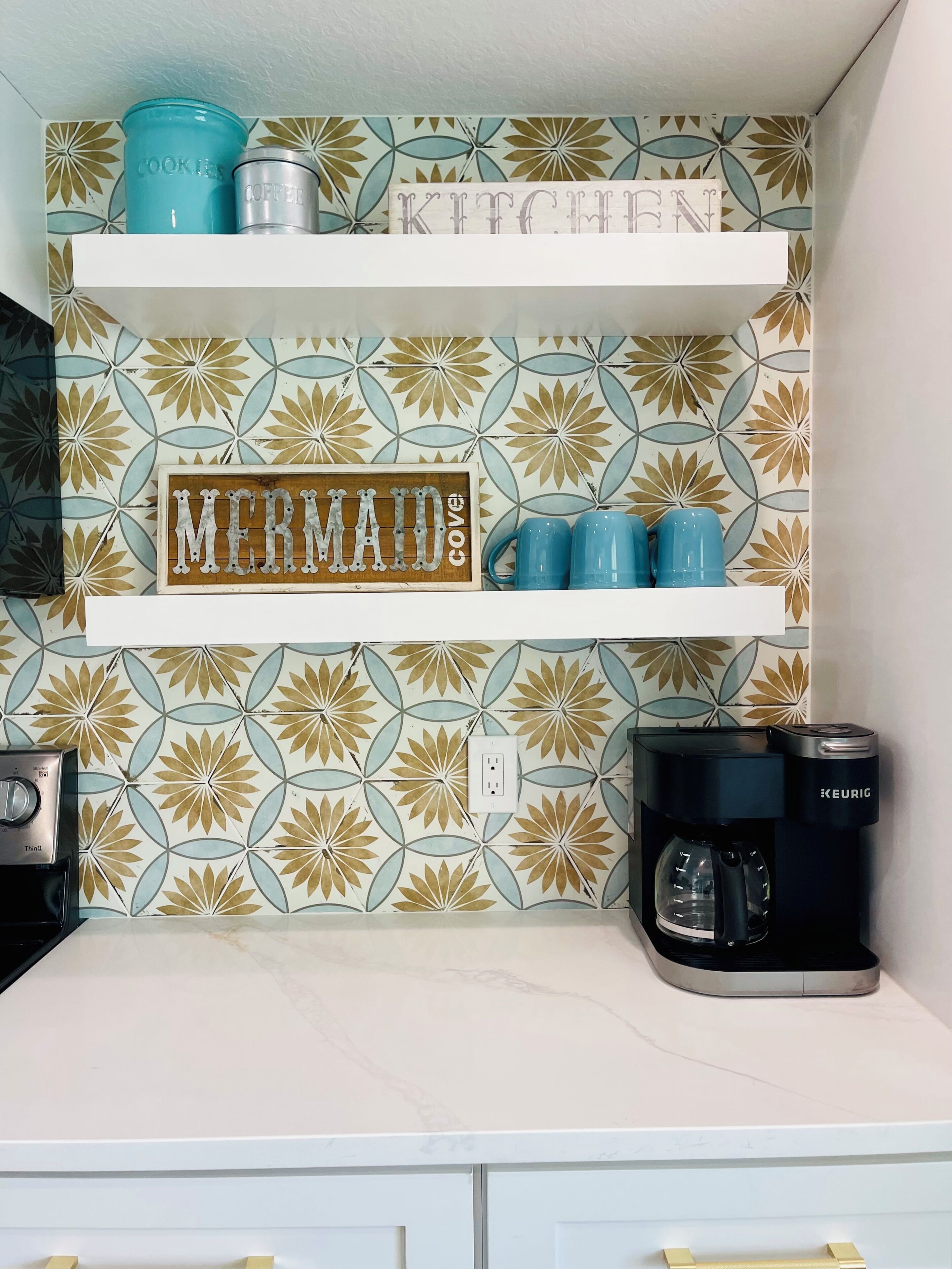 Una cocina con un salpicadero decorativo, una cafetera y una repisa con utensilios de cocina.
