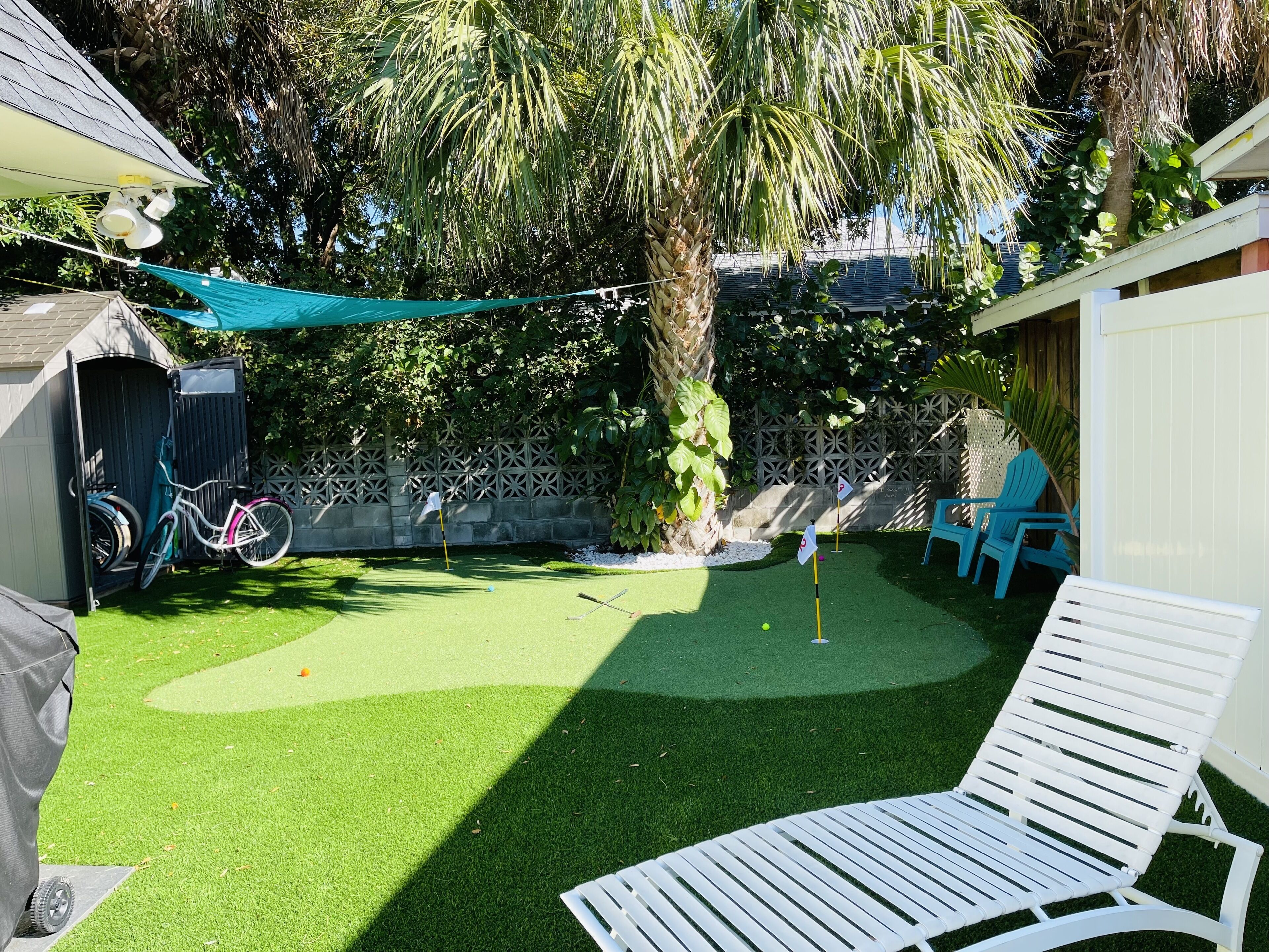 A backyard with artificial grass, a white lounge chair, and a bicycle.
