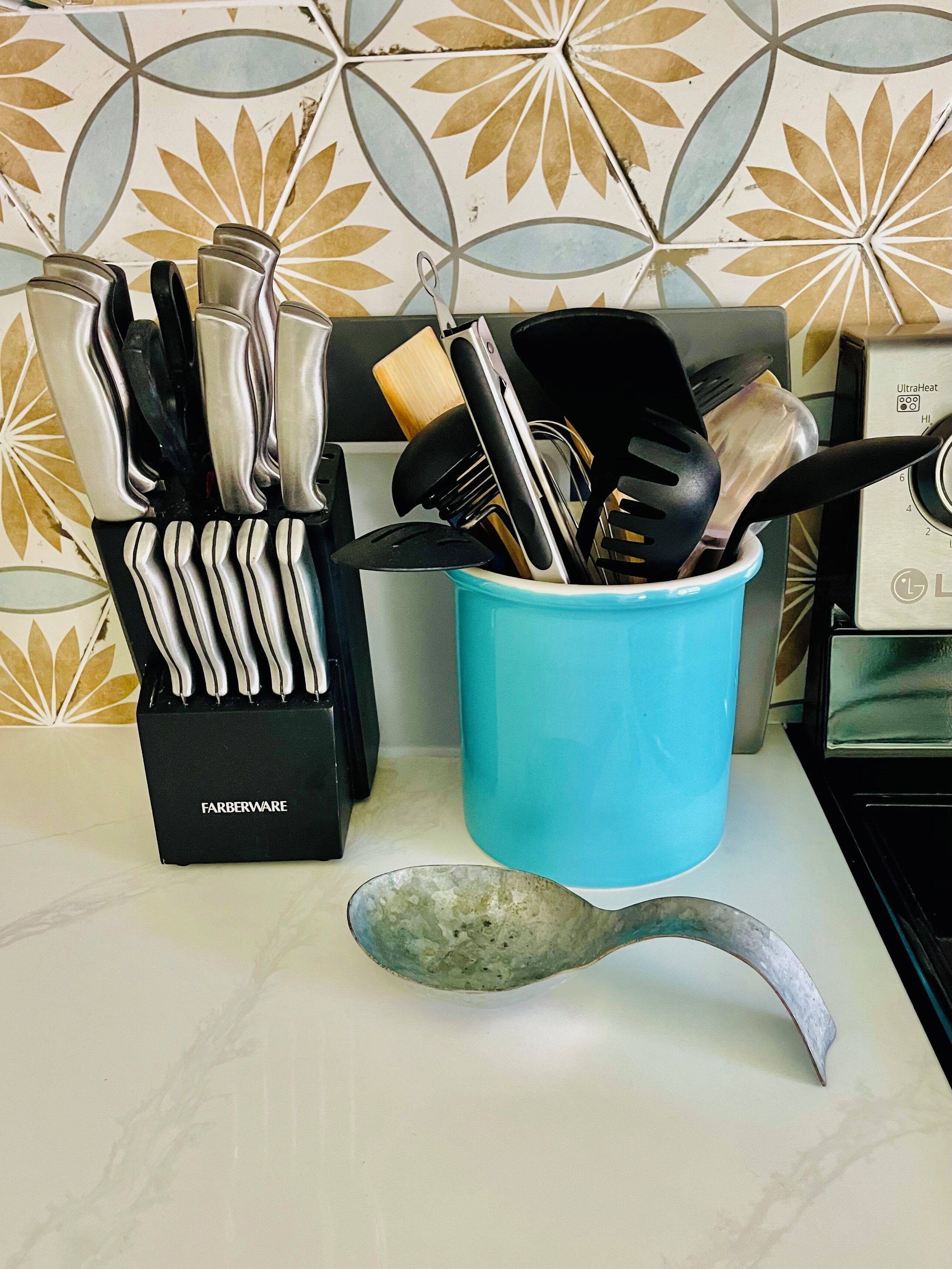 Una encimera de cocina con un bloque de cuchillos, un recipiente azul para utensilios y una cuchara de metal.