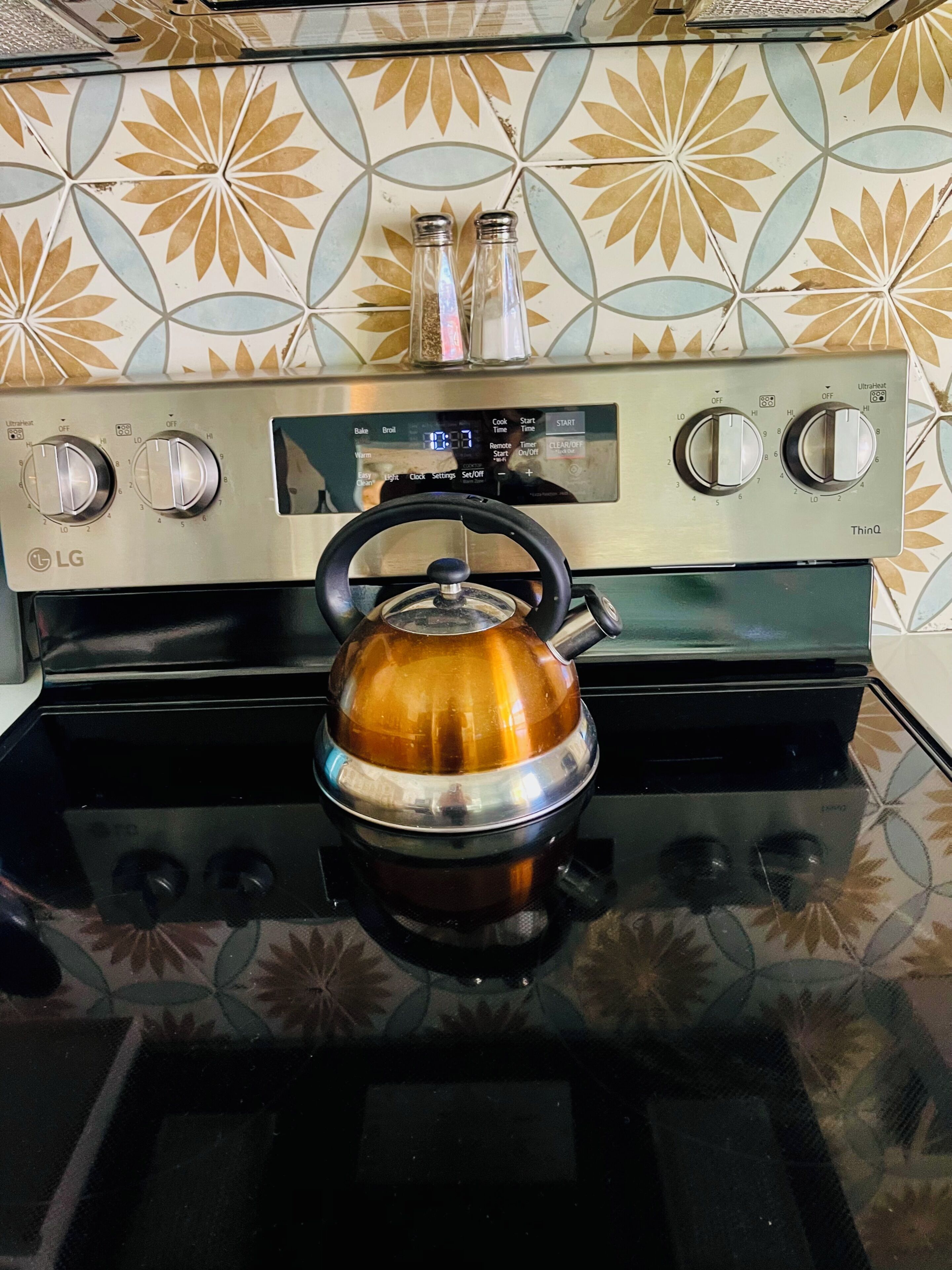 A kitchen with a stove, a kettle, and a patterned backsplash.