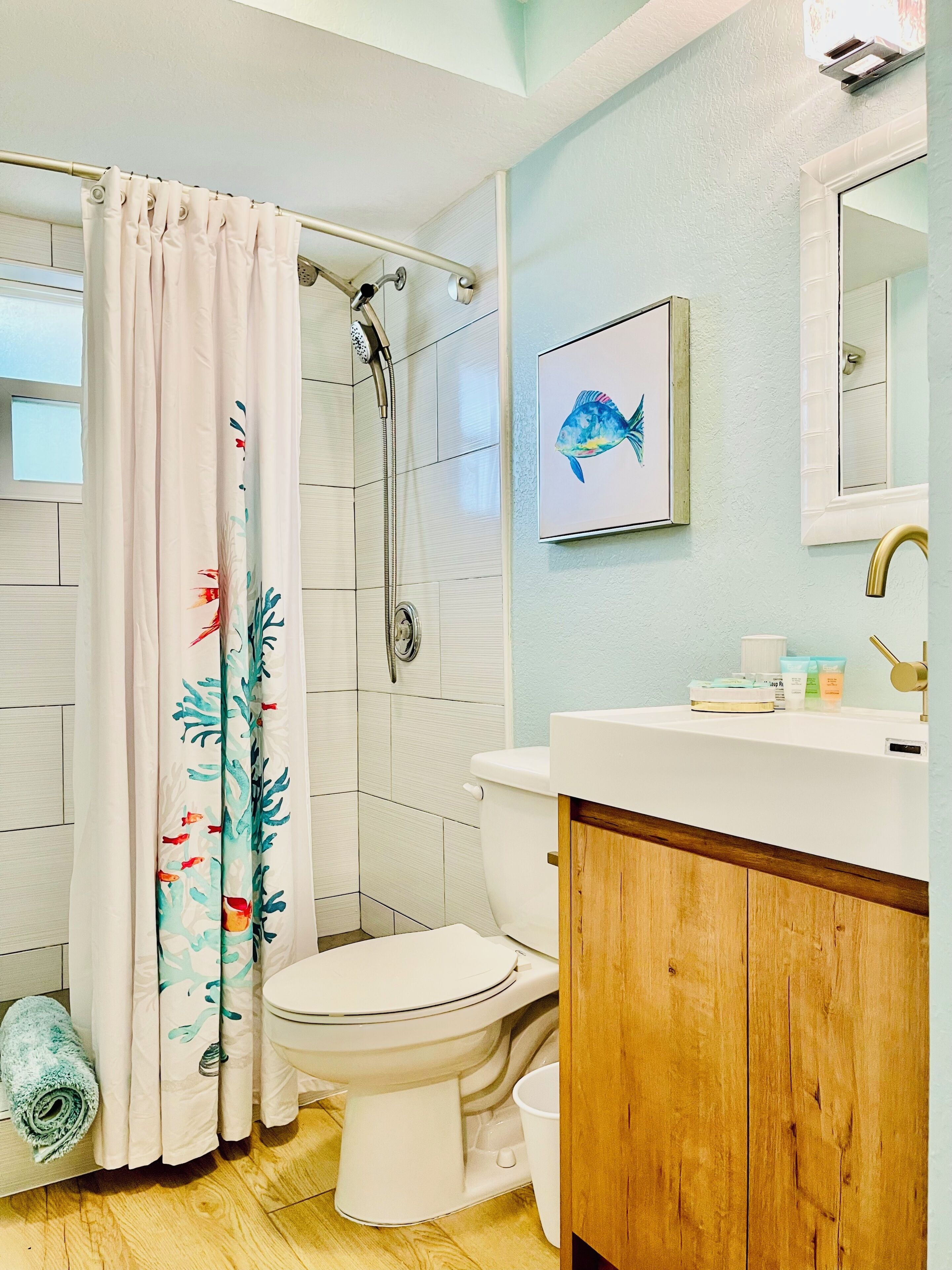 A bathroom with a shower, toilet, sink, and a framed fish painting on the wall.