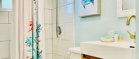 A bathroom with a shower, toilet, sink, and a framed fish painting on the wall.