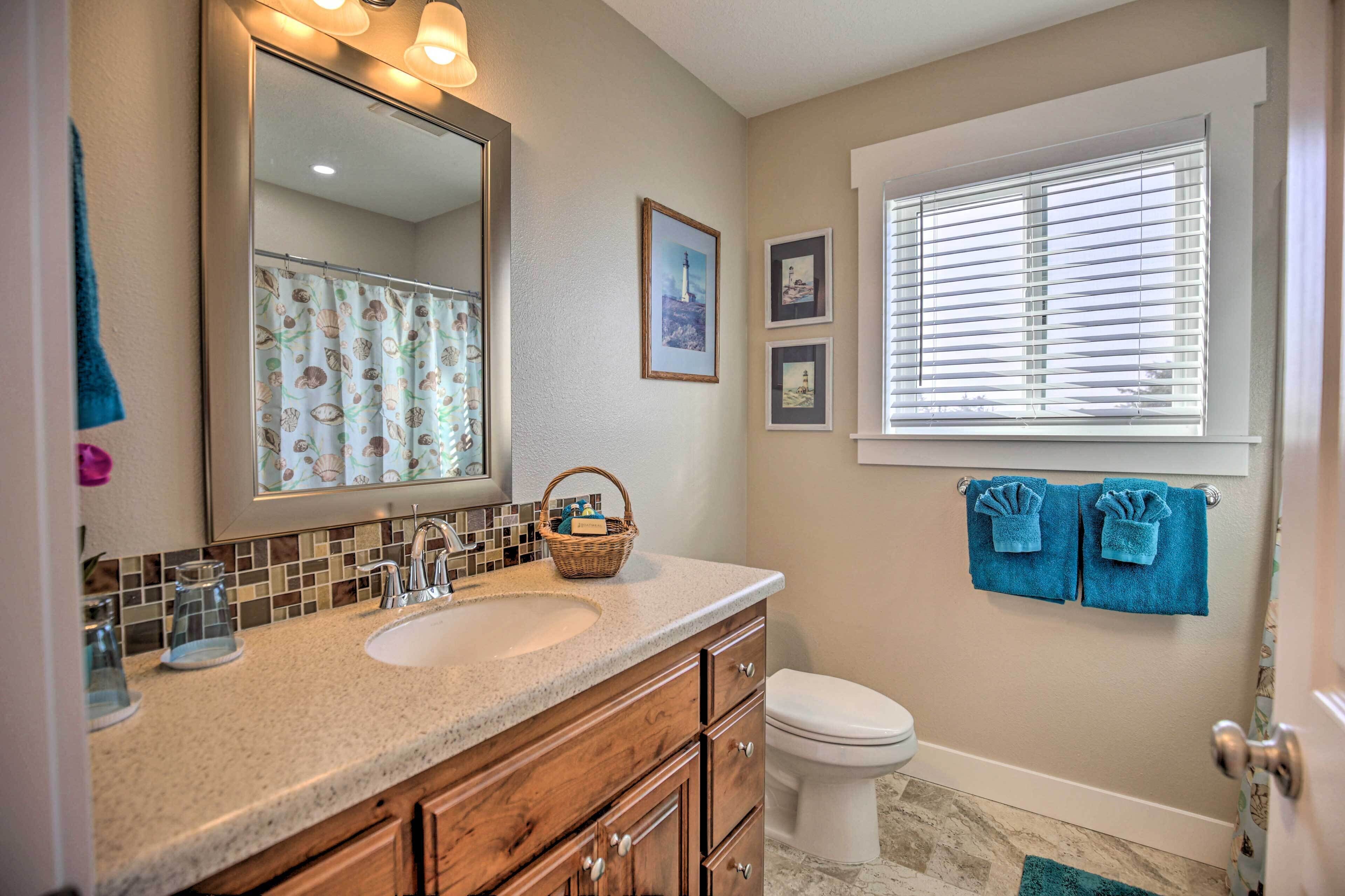 A bathroom with a sink, mirror, and toilet. There are towels hanging on the wall and a window with blinds.
