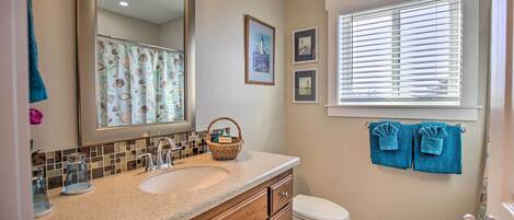 A bathroom with a sink, mirror, and toilet. There are towels hanging on the wall and a window with blinds.