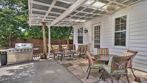 Une terrasse extérieure équipée d’un barbecue, d’une table à manger, de chaises et d’un espace abrité avec un ventilateur de plafond.