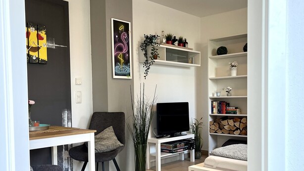 Una sala de estar moderna con una televisión de pantalla plana, una mesa de comedor con sillas, un sofá y una estantería.