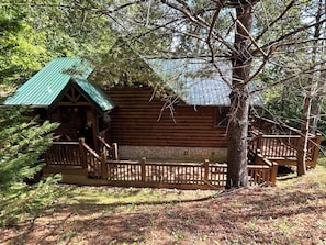 A log cabin with a green roof, wooden deck, and stone foundation.