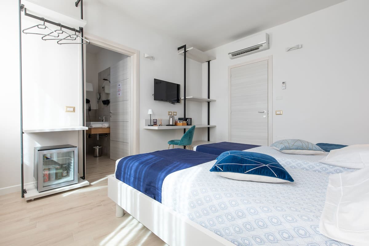A modern bedroom with two beds, a small kitchenette, a TV, and a walk-in closet.