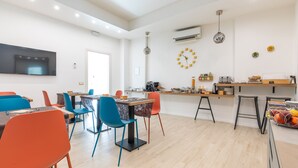 Un comedor moderno con una mesa larga, sillas coloridas y una zona de cocina con taburetes y electrodomésticos.
