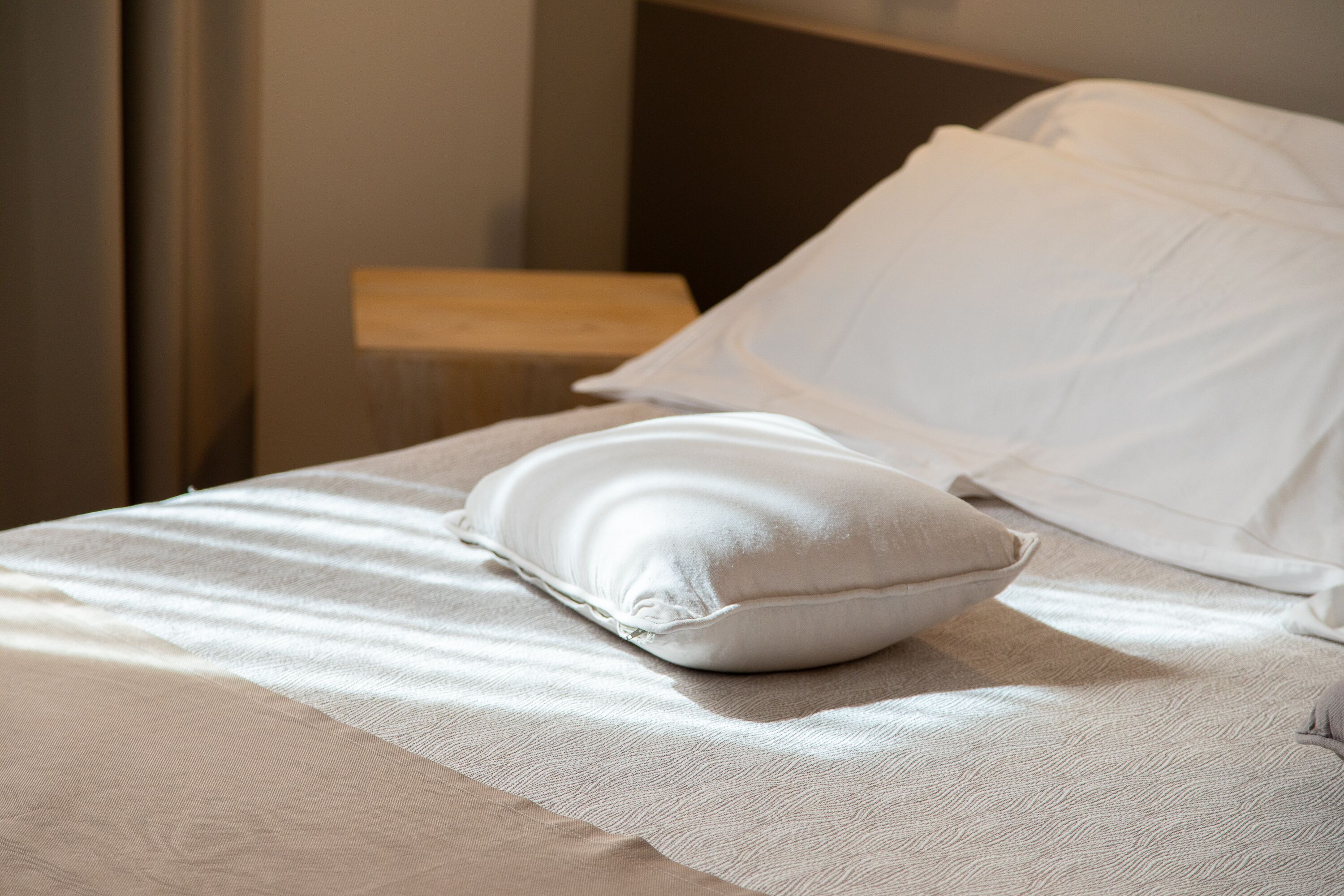 Una cama bien hecha con sábanas y almohadas blancas, un cabecero de madera y una mesita de noche.