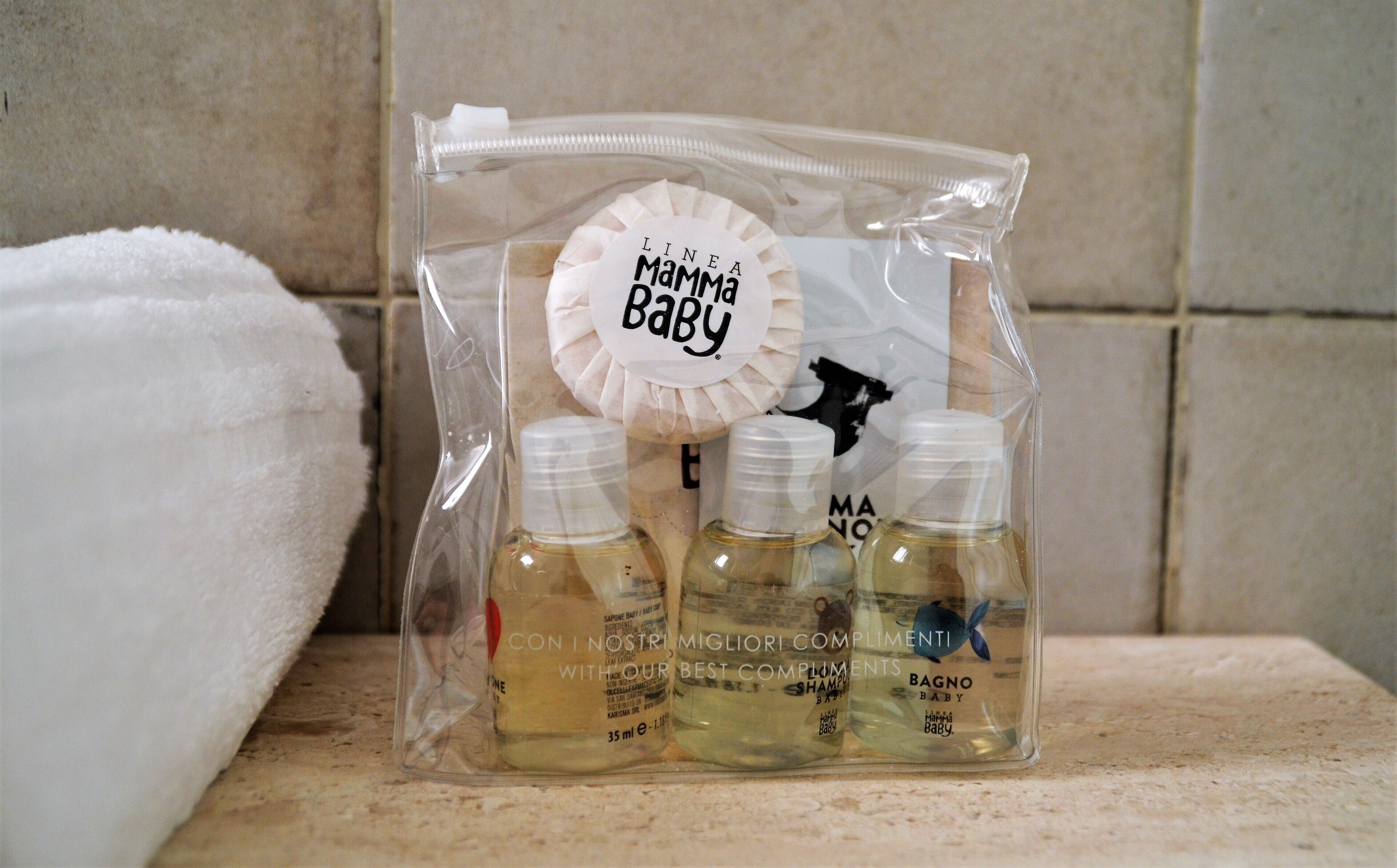 A clear plastic bag containing baby care products, including shampoo and a baby bottle, with a label that reads "LINEA Mamma Baby".