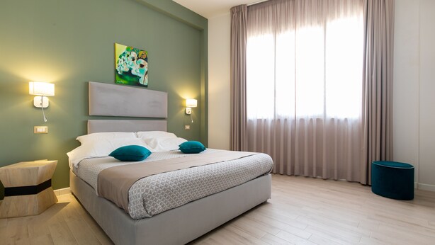 Un dormitorio moderno con una cama grande, dos lámparas de noche, un cuadro en la pared y una ventana con cortinas.