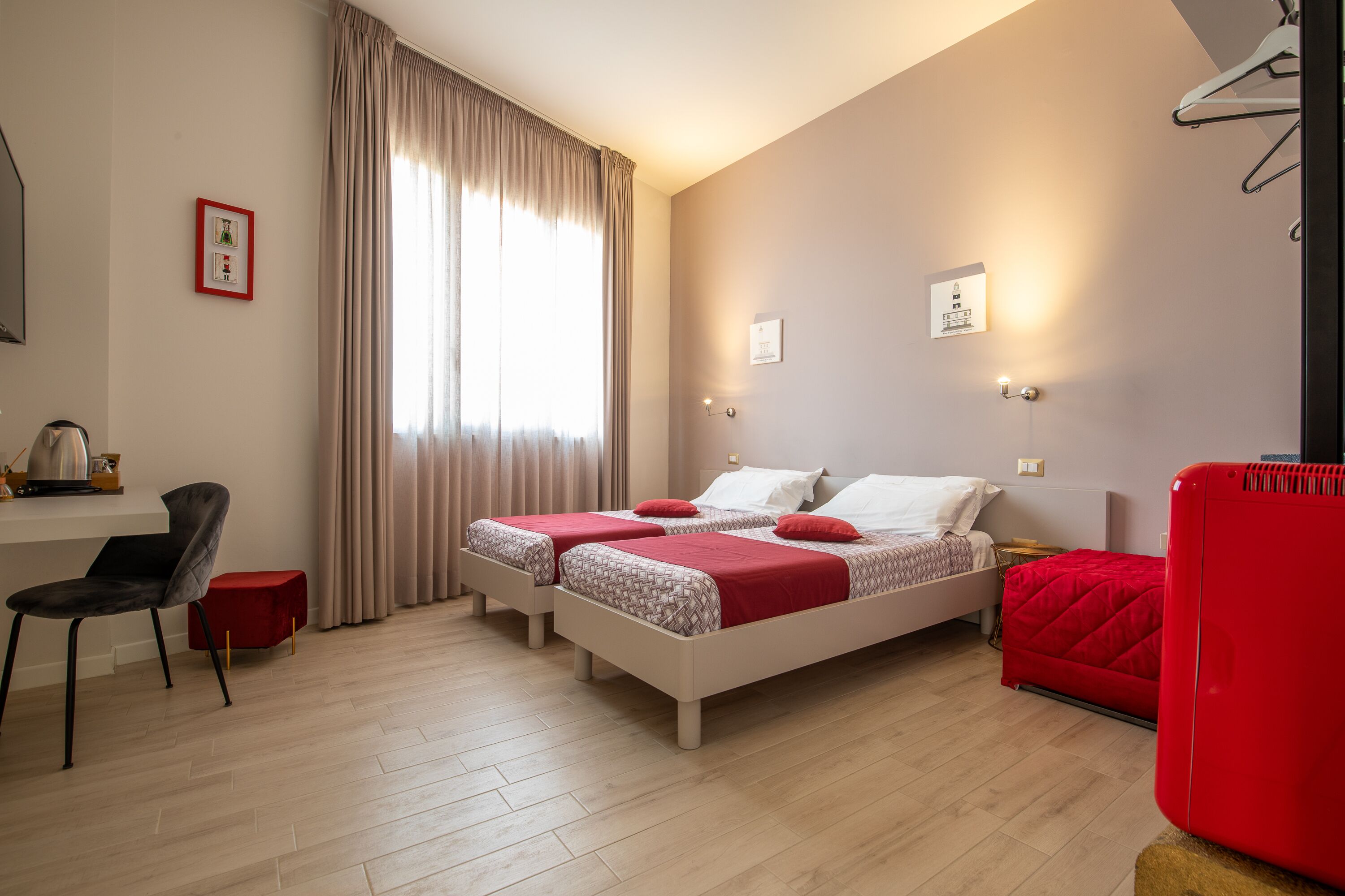 Una habitació d'hotel amb dos llits, una taula de treball, una cadira i un sofà vermell.