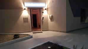 Entrada de hotel con iluminación adecuada, un pequeño jardín y una puerta con el número 99.