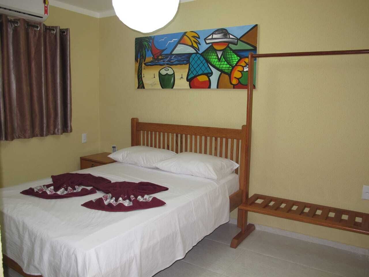 A bedroom with a wooden bed, white bedding, a brown curtain, and a colorful painting on the wall.