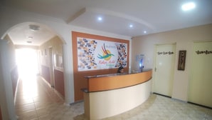 Uma área de recepção de hotel com um balcão curvo, uma placa na parede com o logotipo de um pássaro e um corredor que dá para outros quartos.