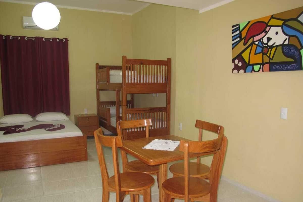 A room with a bed, a dining table with chairs, a bunk bed, and a colorful painting on the wall.