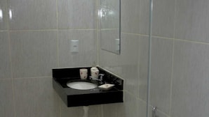 Casa de banho com sanita, cabine de duche com portas de vidro e lavatório com produtos de higiene pessoal sobre bancada preta.
