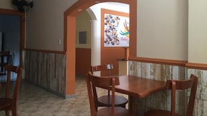 Um corredor com um banco e cadeiras de madeira, piso ladrilhado e uma parede com um cartaz colorido.