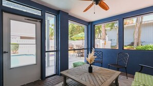 A room with a wooden table, chairs, a ceiling fan, and large windows offering a view of the outside. - 19 Dove St - Large Pool, Short Walk to Beach! (Hilton Head Island)