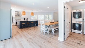 A modern kitchen with a central island, bar stools, and a dining table with chairs. There are two washing machines and a refrigerator visible. - 19 Dove St - Large Pool, Short Walk to Beach! (Hilton Head Island)