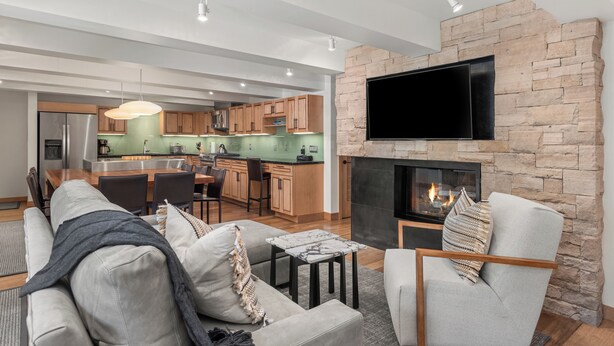A modern living room with a fireplace, a dining area, and a kitchen in the background. - Contemporary Condo in Aspen Core (Aspen)