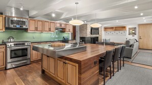 A modern kitchen with wooden cabinets, stainless steel appliances, and a central island with bar stools. - Contemporary Condo in Aspen Core (Aspen)