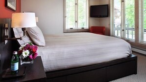 A bedroom with a large bed, a TV mounted on the wall, and a window with blinds. - Contemporary Condo in Aspen Core (Aspen)