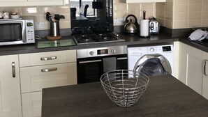 Een moderne keuken met witte kastjes, een roestvrijstalen afzuigkap, een magnetron, een fornuis, een vaatwasser en een spoelbak.