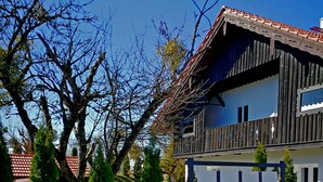 A two-story house with a wooden balcony, surrounded by a well-maintained garden and trees. - Large vacation guest apartment Münsing near Lake Starnberg and the Alps 125m² ground floor + first floor (Münsing)