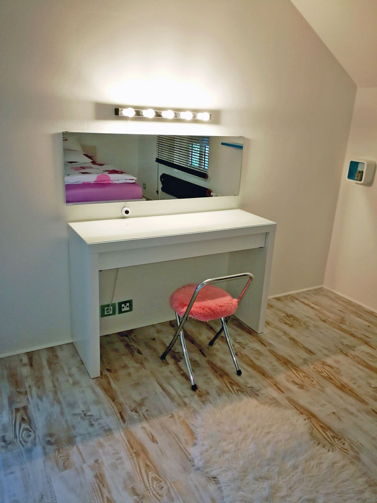 Een ruime, goed verlichte kamer met een make-up hoekje, een spiegel en een roze stoel.
