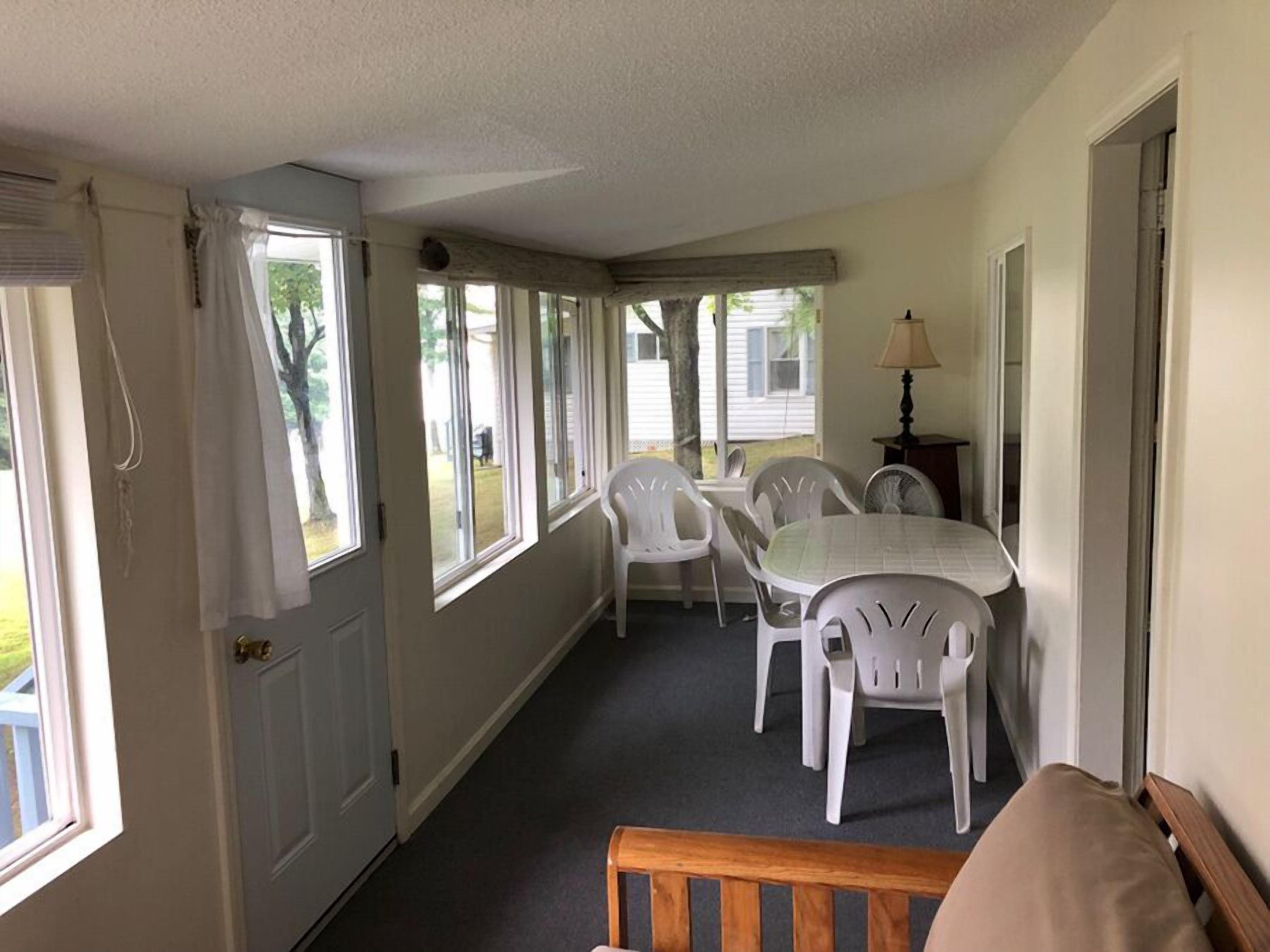 A room with a dining table and chairs, a lamp, and a view of the outdoors through large windows.