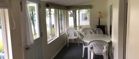 A room with a dining table and chairs, a lamp, and a view of the outdoors through large windows.
