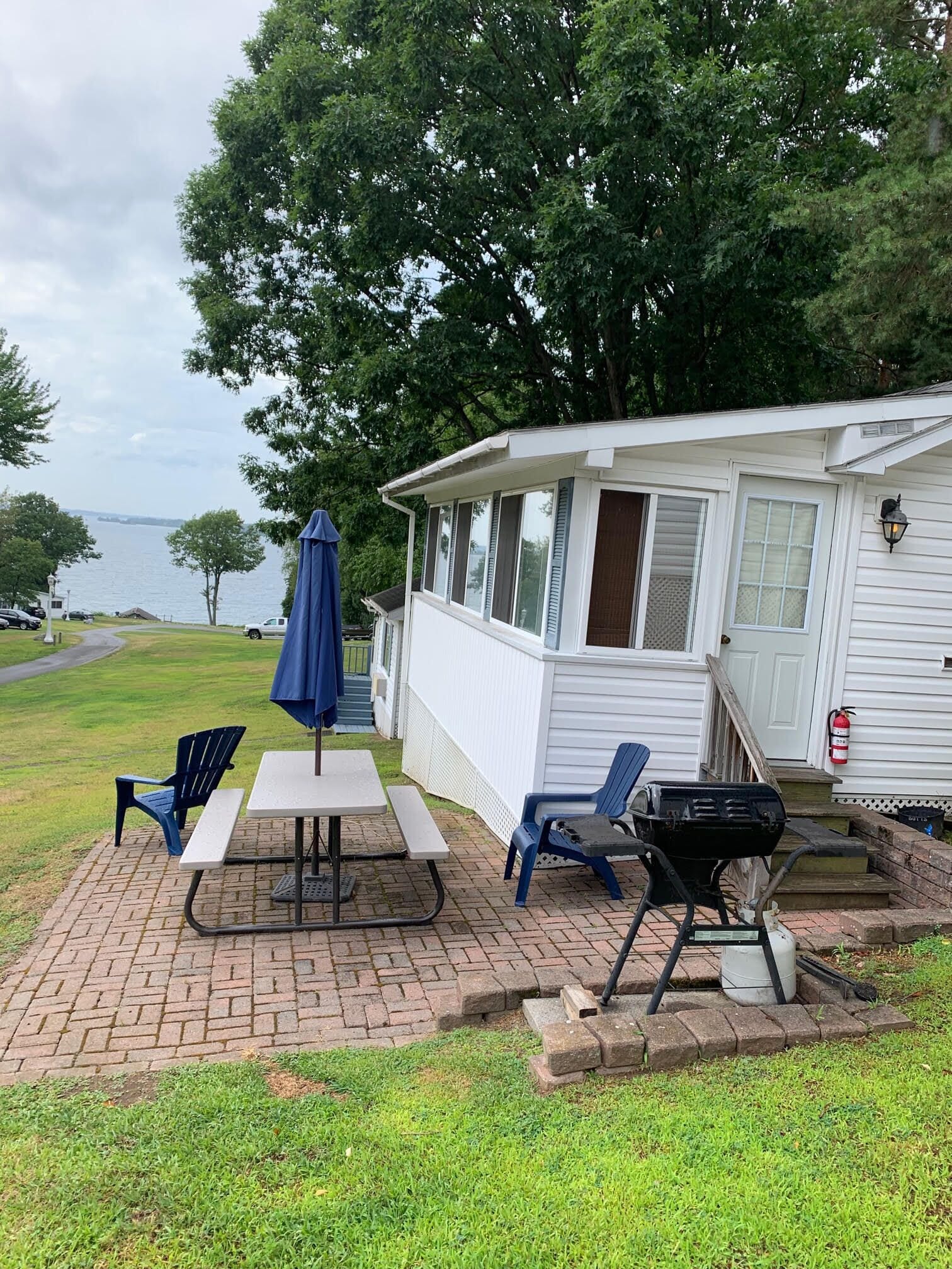 Une terrasse couverte avec des tables et des chaises pour pique-niquer, un barbecue et une vue sur un lac.