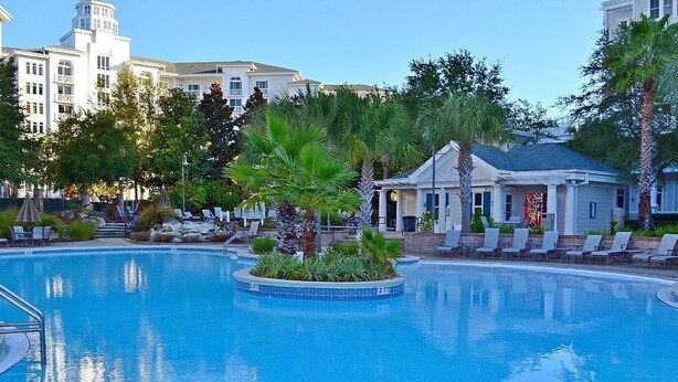 A swimming pool with lounge chairs and palm trees, surrounded by buildings. - Baytowne Wharf - 4th Floor Corner Apartment (Sandestin)