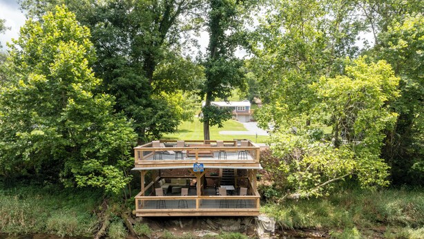 Une terrasse en bois avec des sièges extérieurs, donnant sur une rivière et entourée d’une végétation luxuriante.
