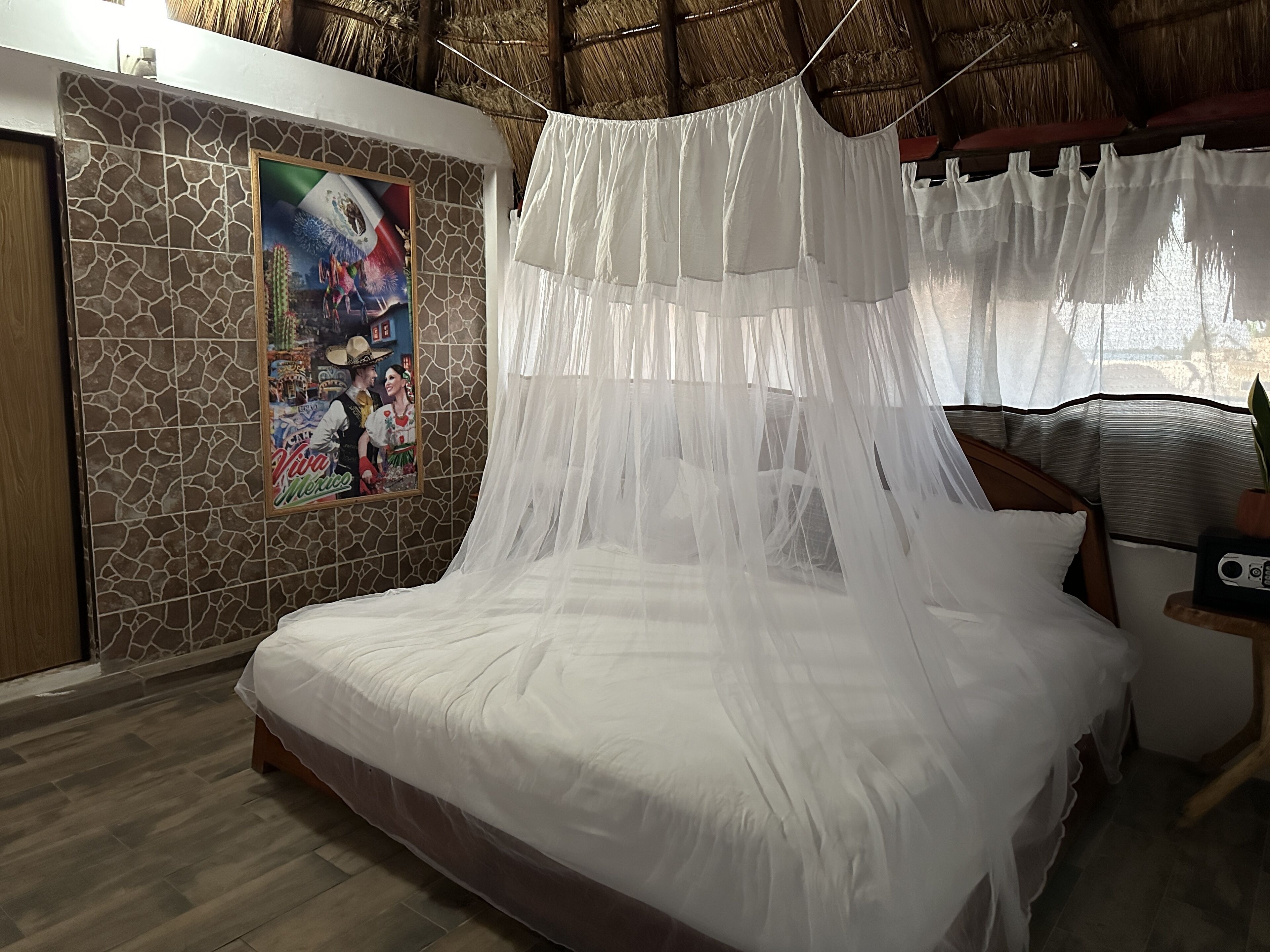 Una cama con dosel blanco, pared de piedra con un mural y suelo de madera.