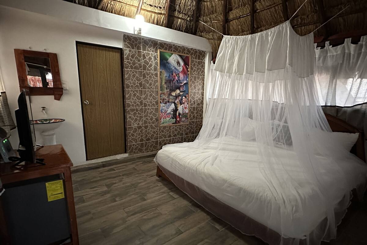 Un dormitorio con cama, mesita de noche, televisor, espejo, puerta y pared decorada con un mural.