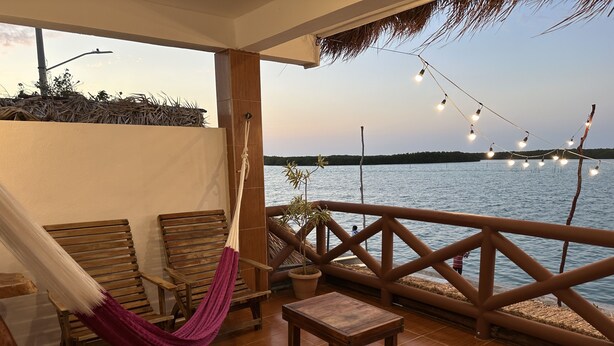 A wooden deck with a hammock, chairs, and a table overlooking a body of water. - Hotel el Faro (Río Lagartos)