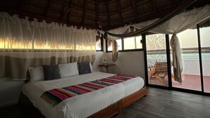 A spacious bedroom with a large bed, a ceiling fan, and a view of the outdoors through large windows. - Hotel el Faro (Río Lagartos)