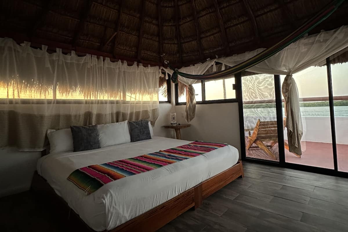 Un dormitorio amplio con una cama grande, un ventilador de techo y vistas al exterior a través de amplias ventanas.