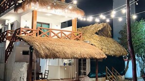 A building with a thatched roof and a balcony, surrounded by string lights. - Hotel el Faro (Río Lagartos)