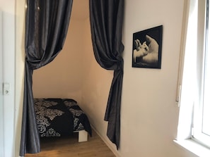 Quarto com cama, cortinas pretas, um quadro na parede e uma janela.