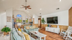 A spacious living room with a large sofa, a coffee table, and a TV. There is a kitchen in the background with wooden cabinets and a window. - 2 min to beach, Private Pool & Hot Tub. Ocean Hill (Corolla)