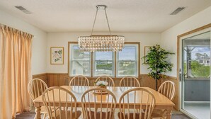 A dining room with a wooden table and chairs, a chandelier, and a view of a house through the window. - 2 min to beach, Private Pool & Hot Tub. Ocean Hill (Corolla)