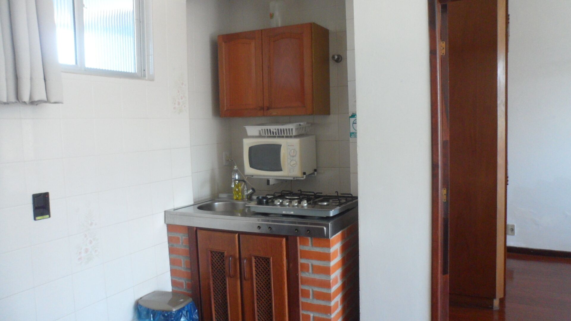 Une cuisine de taille réduite, équipée d’une cuisinière à gaz, d’un four à micro-ondes et de meubles de rangement en bois.