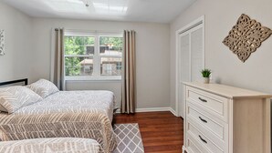 Een slaapkamer met een bed, een dressoir, een plafondventilator, een raam met gordijnen en een decoratief object aan de muur.