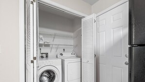 Een wasserette met een wasmachine, droger en een plankenunit.
