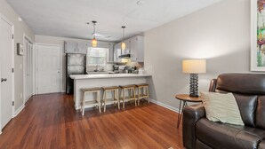 Een moderne keuken met een centraal eiland, barstoelen, hanglampen en een leren bank in een woonruimte met houten vloeren.